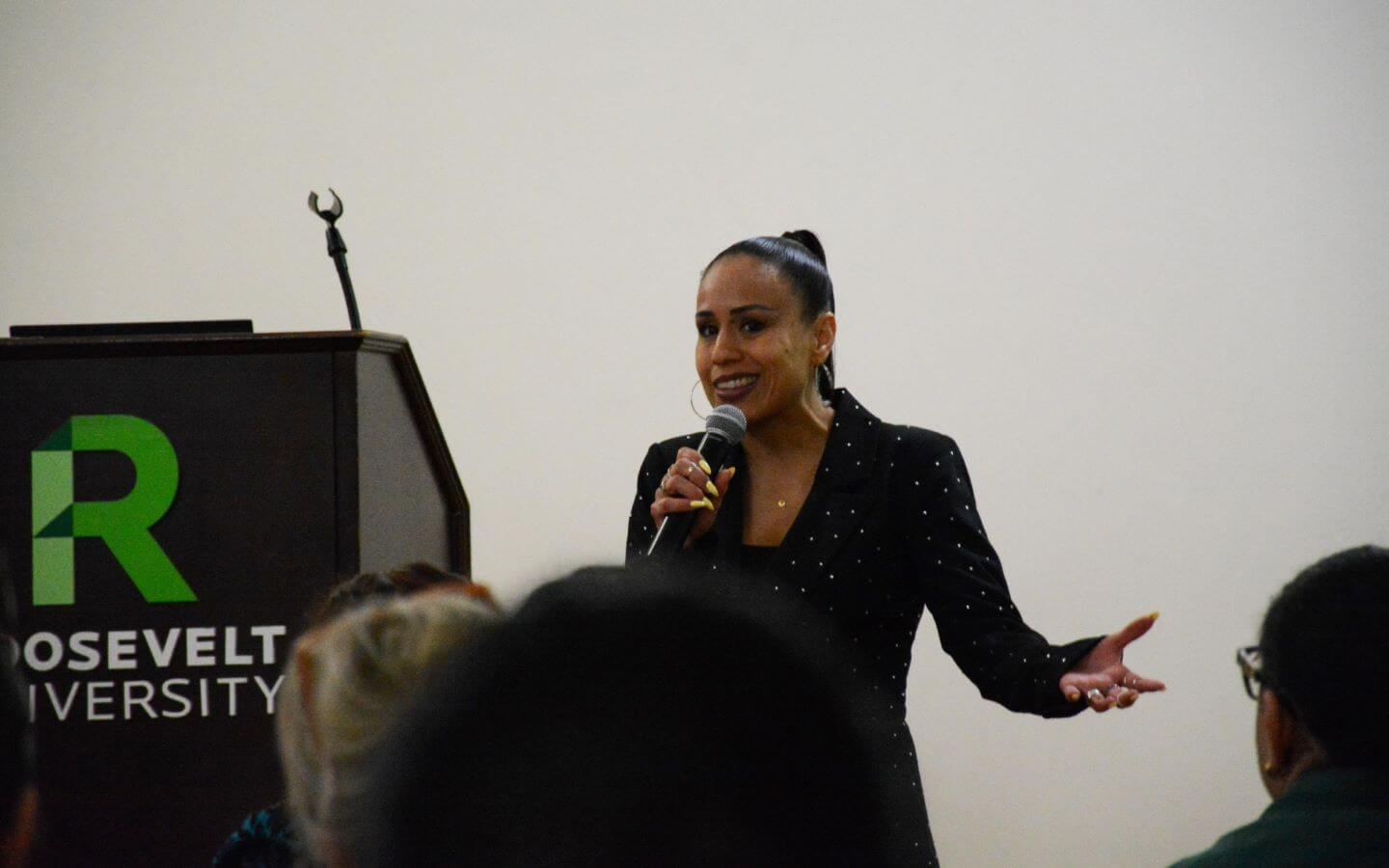 Person standing next to a podium, holding a microphone in front of a group.